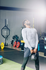 Vertical shot of African American man lifting heavy kettlebell with struggle