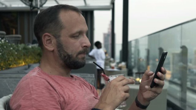Man texting on smartphone and drinking cocktail at luxury bar