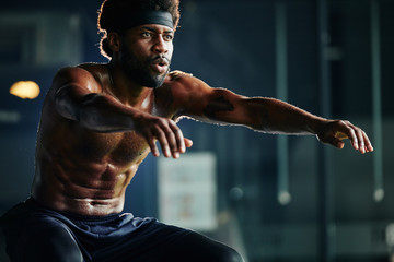 Horizontal shot of topless African American man doing squat exercise in gym