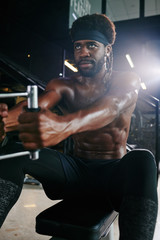 Fototapeta na wymiar Vertical portrait of sporty African American man doing strengthening exercise in gym using fitness machine
