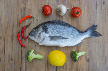 Raw dorado or sea bream fish on wooden table with vegetables