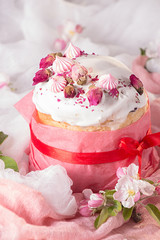 Happy Easter decoration for greeting card. Easter cake with white icing, marshmallows, dry rose and fresh blooming apple flowers and rose color craft paper on gauze background..