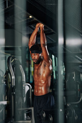 Naklejka premium Vertical shot of handsome black man doing pull-up exercise shirtless in gym