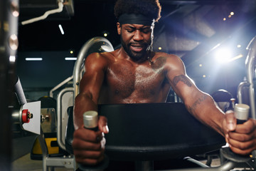 Fototapeta na wymiar Horizontal shot of masculine black guy doing strength exercise using gym equipment