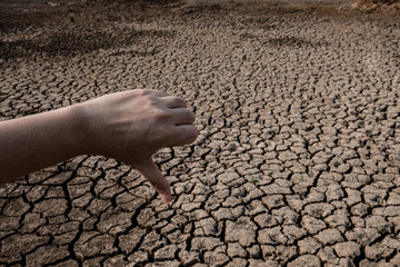 Women hand thumbs down on cracked and dry soil in arid areas landscape