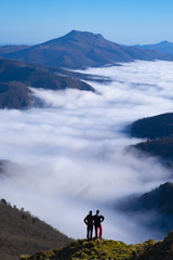 Obraz premium Two mountaineers with sea of clouds and Mount Larun in the background from the natural park of Aiako Harriak, Euskadi Pyrenees