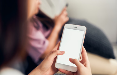 Woman hand holding smartphone with blank screen on sofa in house with friends. Take your screen to...