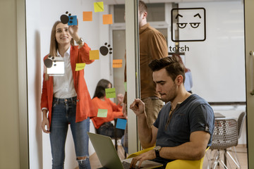 Obraz premium Startup business people group working everyday job at modern coworking office space. business, startup, planning and people concept - happy creative team writing on stickers at office glass board