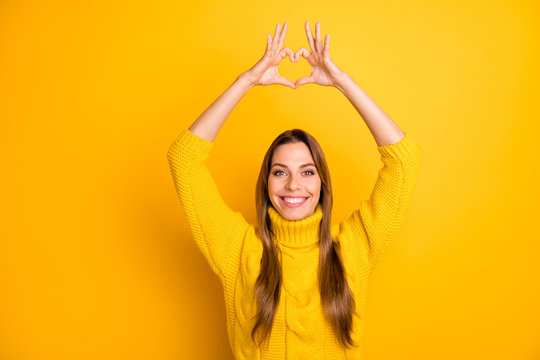 Portrait of positive cheerful girl want celebrate valentine cupid day date with her boyfriend make heart from fingers passionate love sign wear soft jumper isolated yellow color background