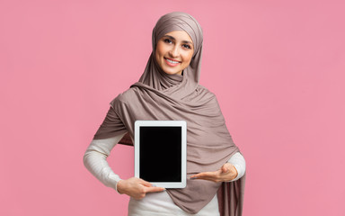 Muslim girl in hijab pointing at digital tablet with black screen