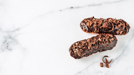 Set of homemade eclairs with chocolate on white marble background. Close up view of delicious healthy profitroles with chocolate glaze. Copy space for text or design. Banner