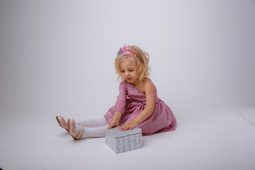 a blonde girl with a gift in a Princess dress sits on a white background
