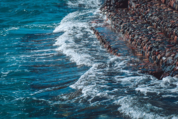 Photo of beautiful clear turquoise sea ocean water surface with ripples and bright splash on stone seascape background, horizontal picture