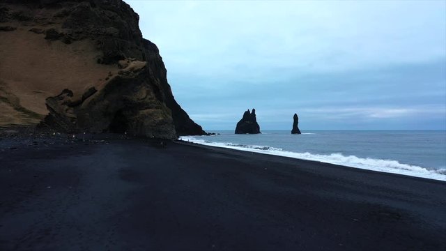 4K Drone Shot Tracking Over The Black Sand Beach In Iceland, Violent Waves Over-Cast. Famous Black Sand Beach In Iceland South Of Iceland, Cloudy Day. Big Rock Cliffs 