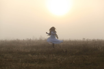 Fototapeta na wymiar Girl dancing in a meadow, the sun rises, there is a fog