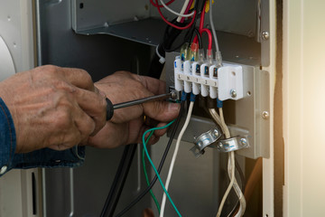 A man's hand uses a screwdriver to connect the electrical wiring inside the air conditioner cabinet.