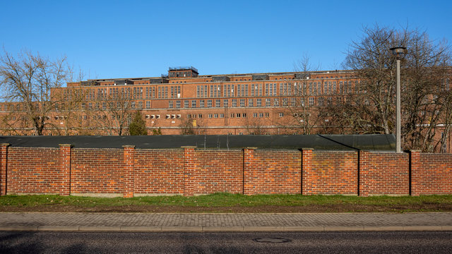 Germany, Saxony-Anhalt, Vockerode: Street view of big old defunct shut down former Vockerode lignite power plant building with brick stone facade, no chimneys and blue sky - concept energy lost place