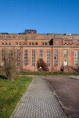 Naklejka premium Germany, Saxony-Anhalt, Vockerode: Street view of big old defunct shut down former Vockerode lignite power plant building with brick stone facade, no chimneys and blue sky - concept energy lost place