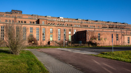 Germany, Saxony-Anhalt, Vockerode: Street view of big old defunct shut down former Vockerode lignite power plant building with brick stone facade, no chimneys and blue sky - concept energy lost place