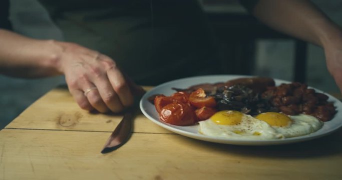 Young woman bringing plate of traditional english breakfast to the dining table