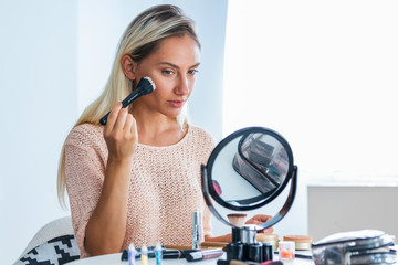 Beauty woman applying makeup. Beautiful girl looking in the mirror and applying cosmetic with a big brush. Girl gets blush on the cheekbones. Powder, rouge