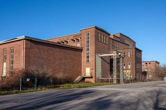 Germany, Saxony-Anhalt, Vockerode: Street view of big old defunct shut down former Vockerode lignite power plant building with brick stone facade, no chimneys and blue sky - concept energy lost place