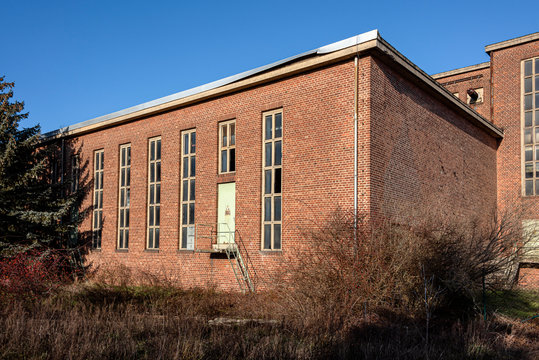 Germany, Saxony-Anhalt, Vockerode: Street view of big old defunct shut down former Vockerode lignite power plant building with brick stone facade, no chimneys and blue sky - concept energy lost place