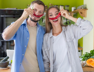 Happy millennial couple playing with pepper slices while cooking