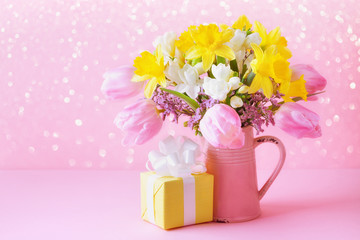 Beautiful spring flowers in vase and gift against pink background. Mothers or Woman day greeting card.