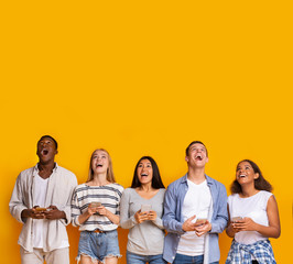 Group of surprised students with smartphones over yellow background