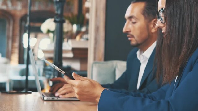 Two businesspeople in deep blue suits are working on laptop and tablet, sitting in coffee shop. Side view. Crop. Close up. Copy space.