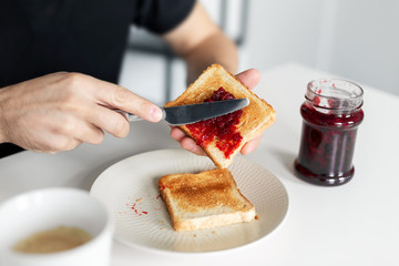 The guy has breakfast with toast with jam.