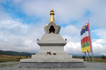 Granite stupa of Enlightenment and Buddhist flags against cloud sky background