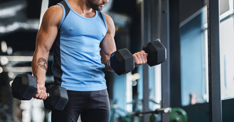 Muscular athlete picking up dumbbells at gym