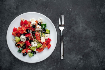 Greek salad in a white plate on a stone background with copy space for your text
