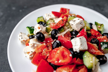 Greek salad in a white plate on a stone background