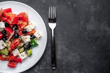 Greek salad in a white plate on a stone background with copy space for your text