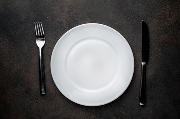 white plate with  fork and knife on a stone background