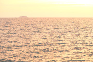 The seaside at sunset has dark shadows in the form of mountains.