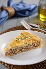 A slice of tuna fish pie with a crispy golden-brown crust, on a white plate with fork and knife on the background.