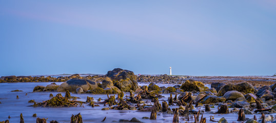 Rocky sea coast shoreline with distant lighthouse.