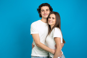 Smiling couple in white t-shirts embracing isolated on blue background