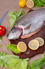 Raw fresh unprepared salmon fish on a wooden board with ingredients for cooking. Lemon, lettuce, tomatoes. Mediterranean cuisine.