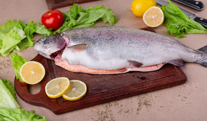 Raw fresh unprepared salmon fish on a wooden board with ingredients for cooking. Lemon, lettuce, tomatoes. Mediterranean cuisine.