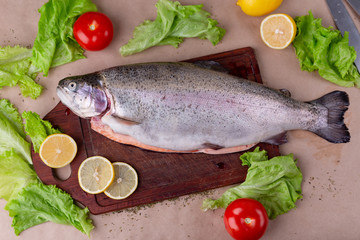 Raw fresh unprepared salmon fish on a wooden board with ingredients for cooking. Lemon, lettuce, tomatoes. Mediterranean cuisine, top view, flat lay.