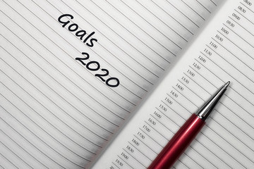 Text 2020 goals on notebook with pen on white background. Top view with copy space for input the...