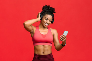 Happy black fitness girl choosing music on smartphone for exercising