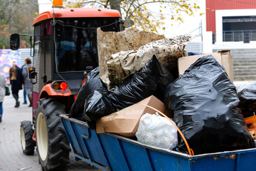 The tractor carries garbage in plastic bags and cardboard boxes in the park.