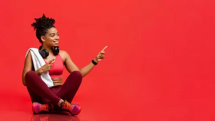 Foto op Plexiglas Cheerful fitness model sitting on floor, pointing at free space © Prostock-studio