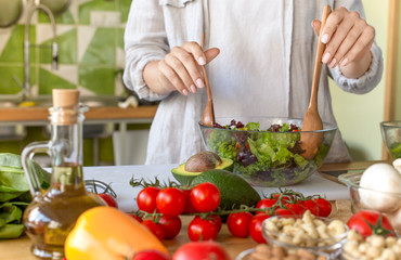 Woman cooking healthy food in the kitchen and mixing fresh salad
